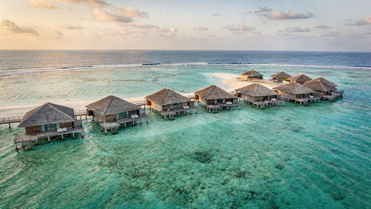Overwater villas on stilts above a shallow turquoise lagoon at first light in the Maldives