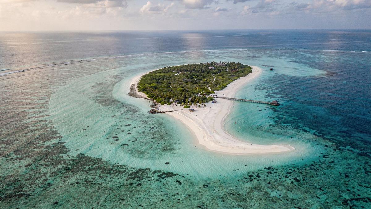 Aerial view of a small Maldives island ringed by pale reef water and a timber jetty